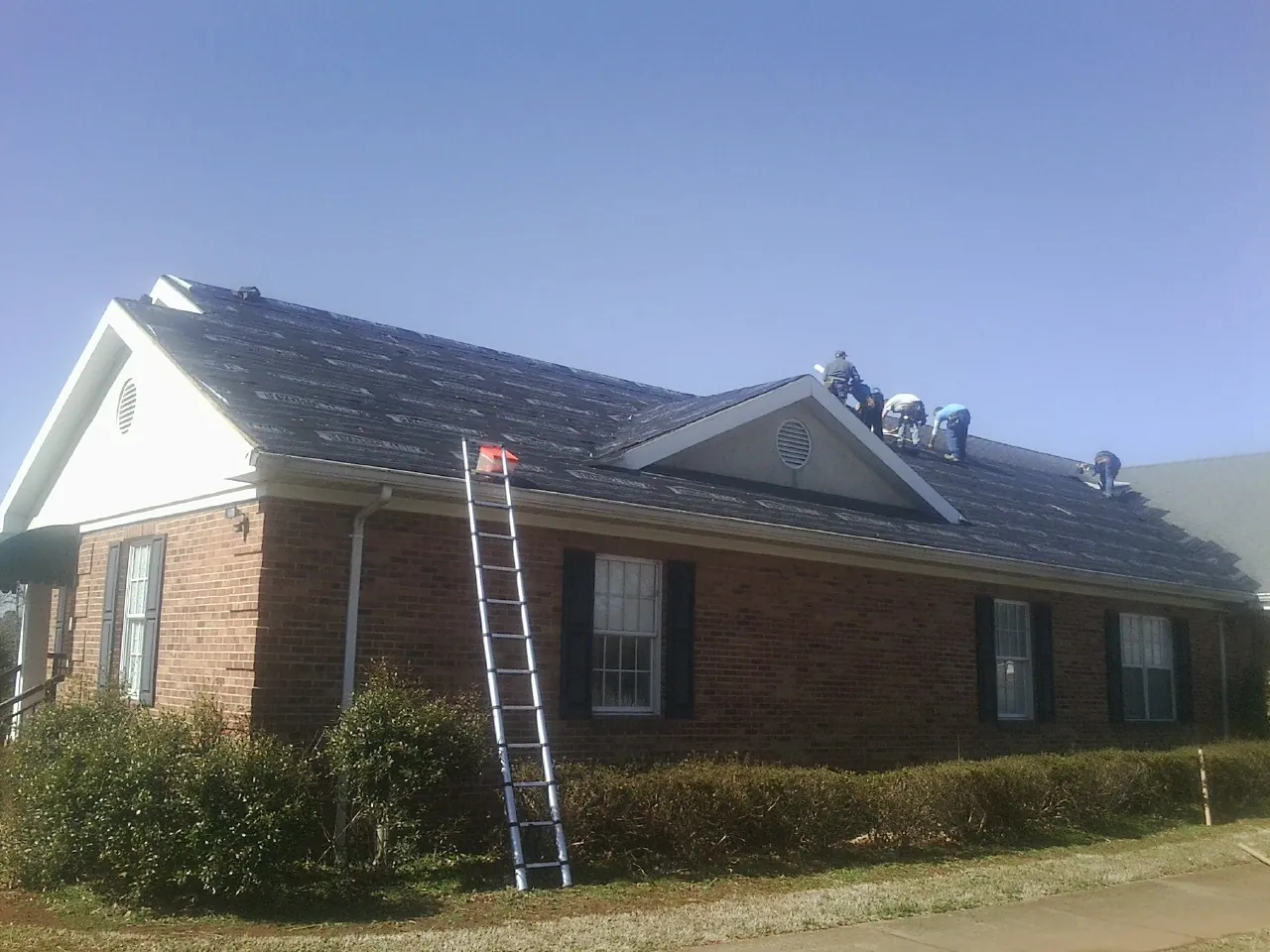 Crew tearing shingles off a brick ranch roof with a ladder set — Metal Roof Repair work by our crew in Entriken