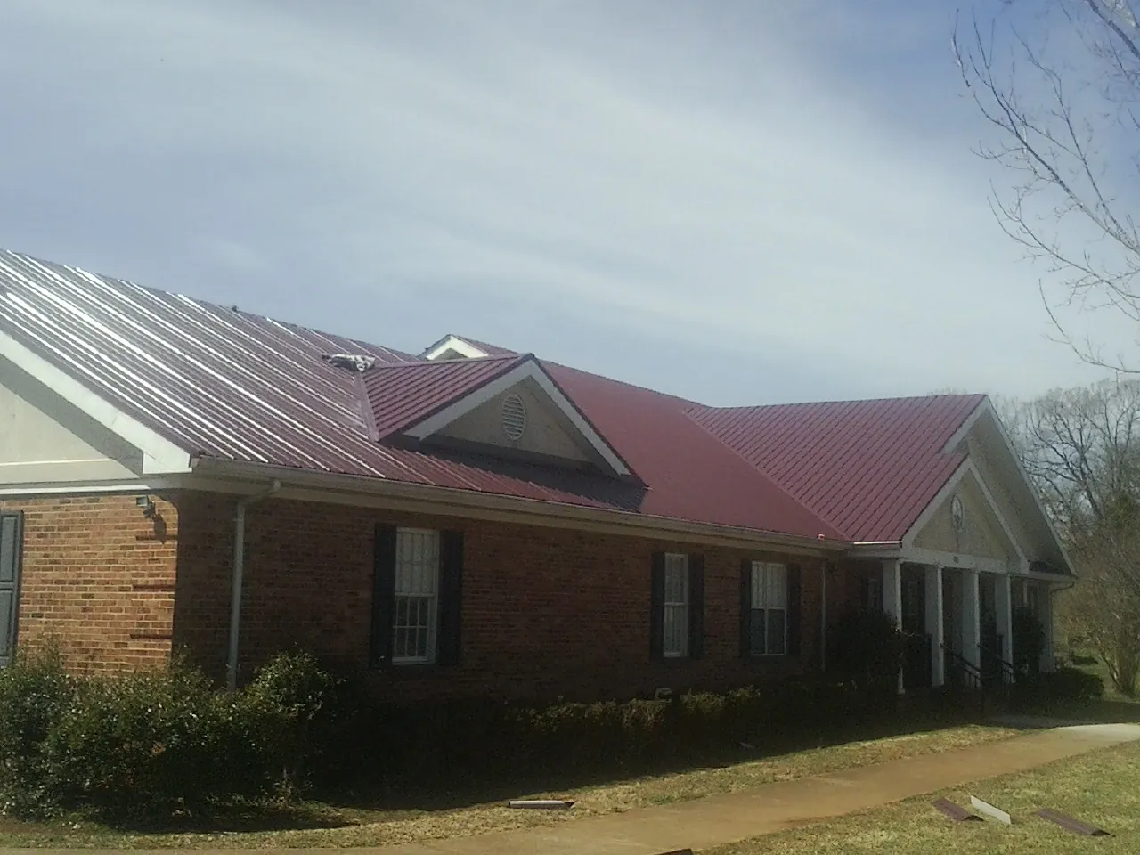 Red metal roof with gabled entries on a long brick building, from a Hail Damage Roof Repair job in Entriken