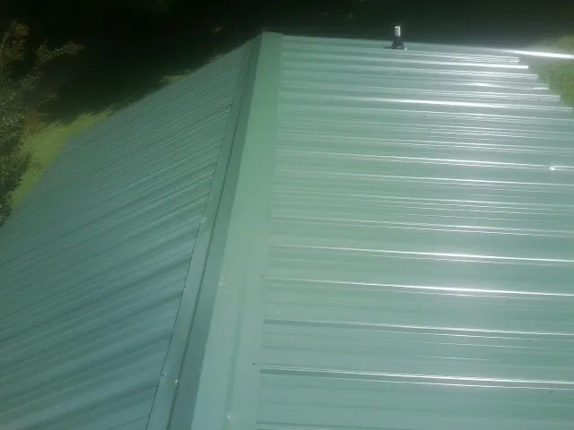 New green metal panels meeting at the ridge of a roof — Flat Roof Repair work by our crew in Entriken