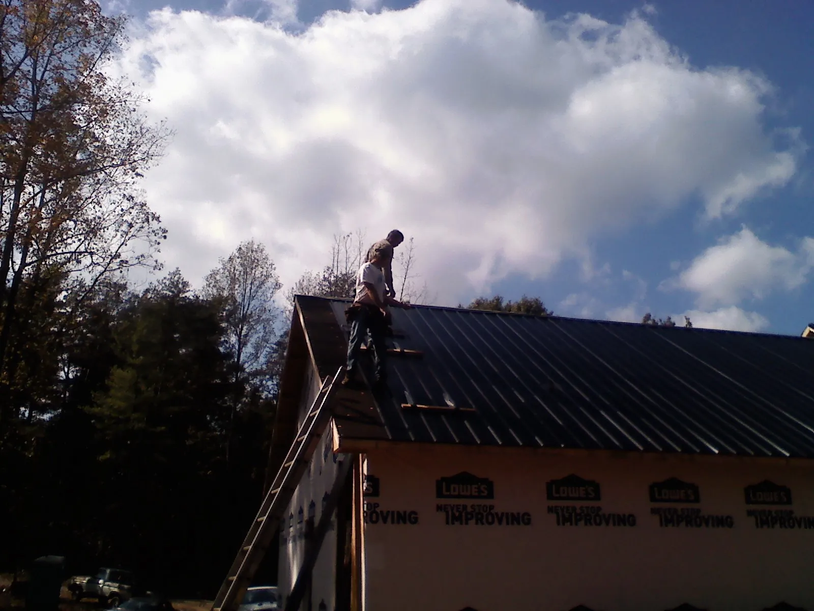 Roofer fastening dark metal panels high against a cloudy sky, from a Roof Inspection job in Entriken