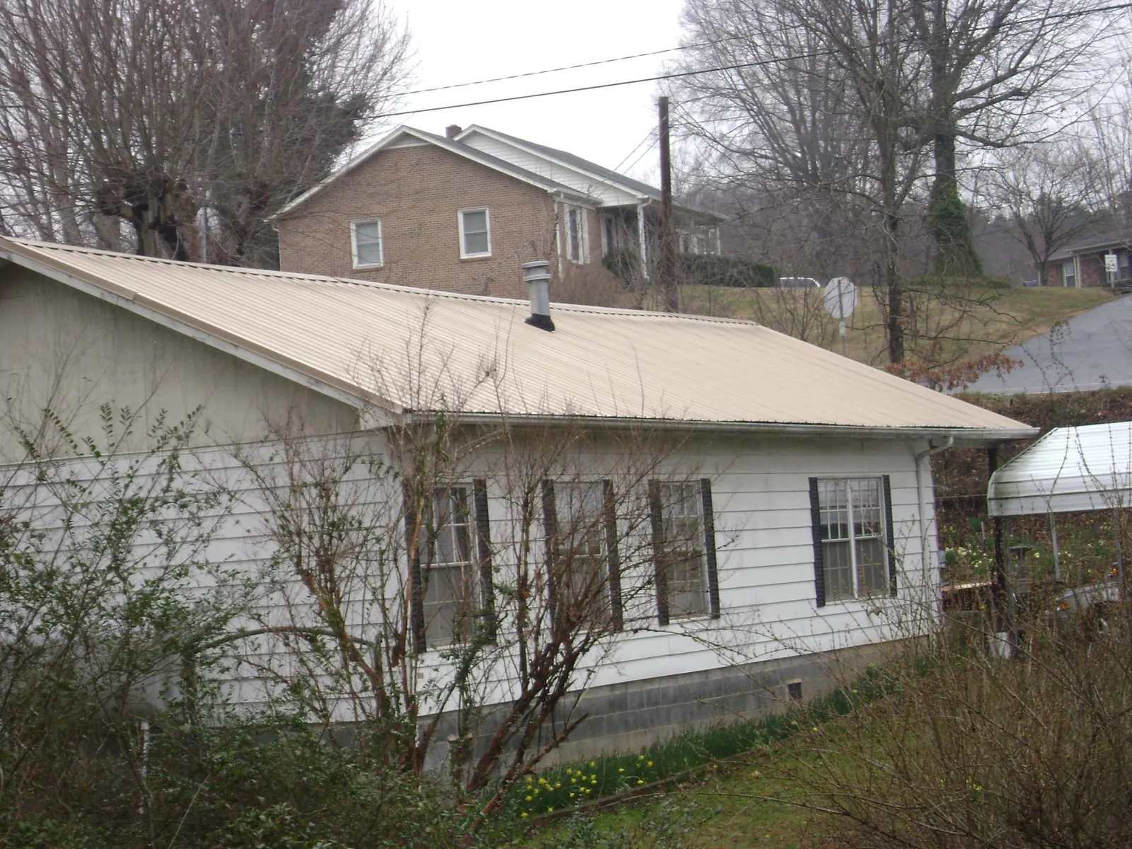 Tan metal roof on a white sided house set into a hillside — Commercial Roofing by Roofing Brothers in Entriken